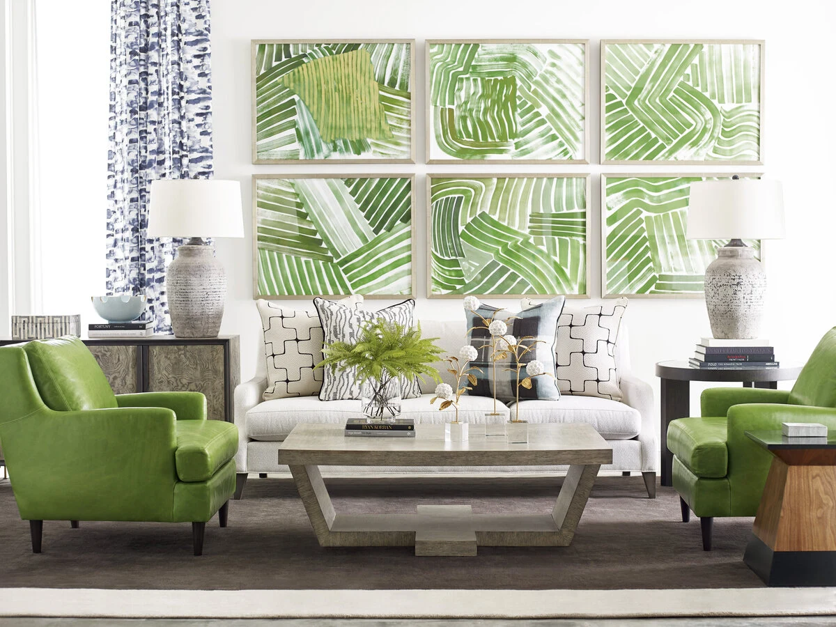 A bright living room with a white upholstered sofa, green accent chairs, a gray wood coffee table, and a bold botanical grid artwork displayed above on the wall.