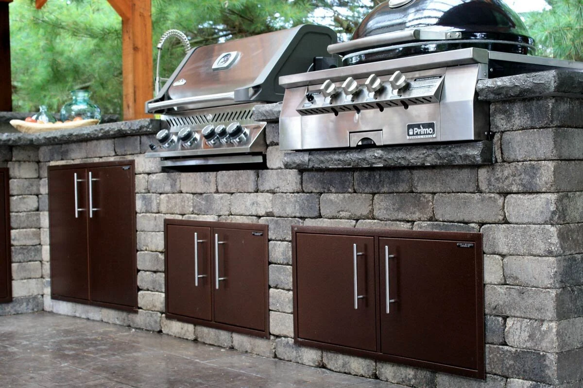 Custom outdoor kitchen with stainless steel grill and dark cabinetry on a warm stone patio. Shop outdoor kitchens near Post Falls, ID.