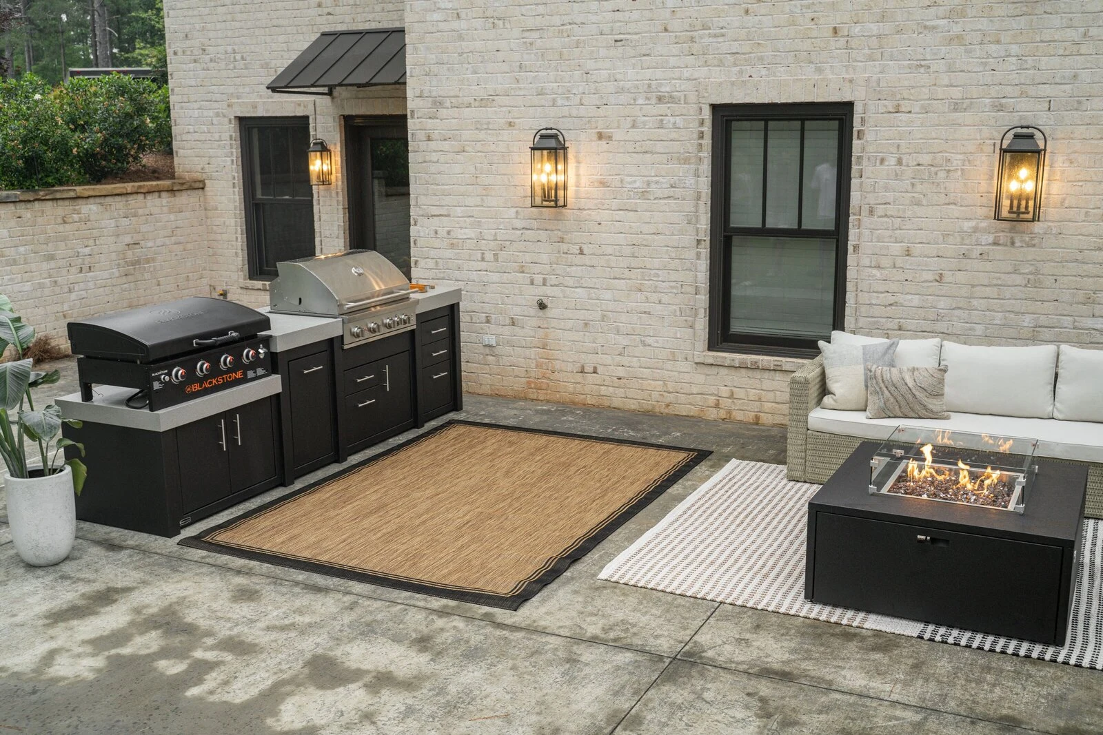 Custom outdoor kitchen with a built-in grill and griddle next to a fire table and outdoor sofa.
