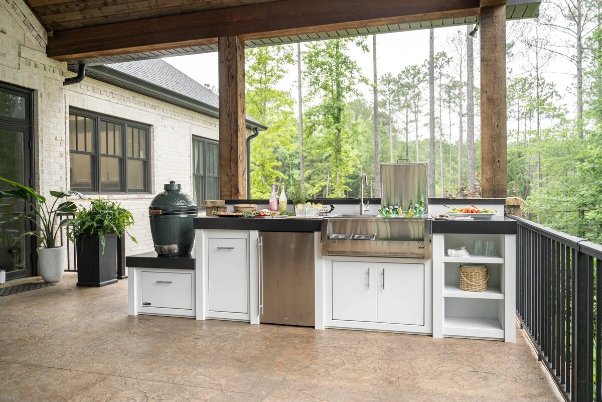 Custom outdoor kitchen with covered patio, stainless steel grill, and lush greenery. Visit our Post Falls showroom.