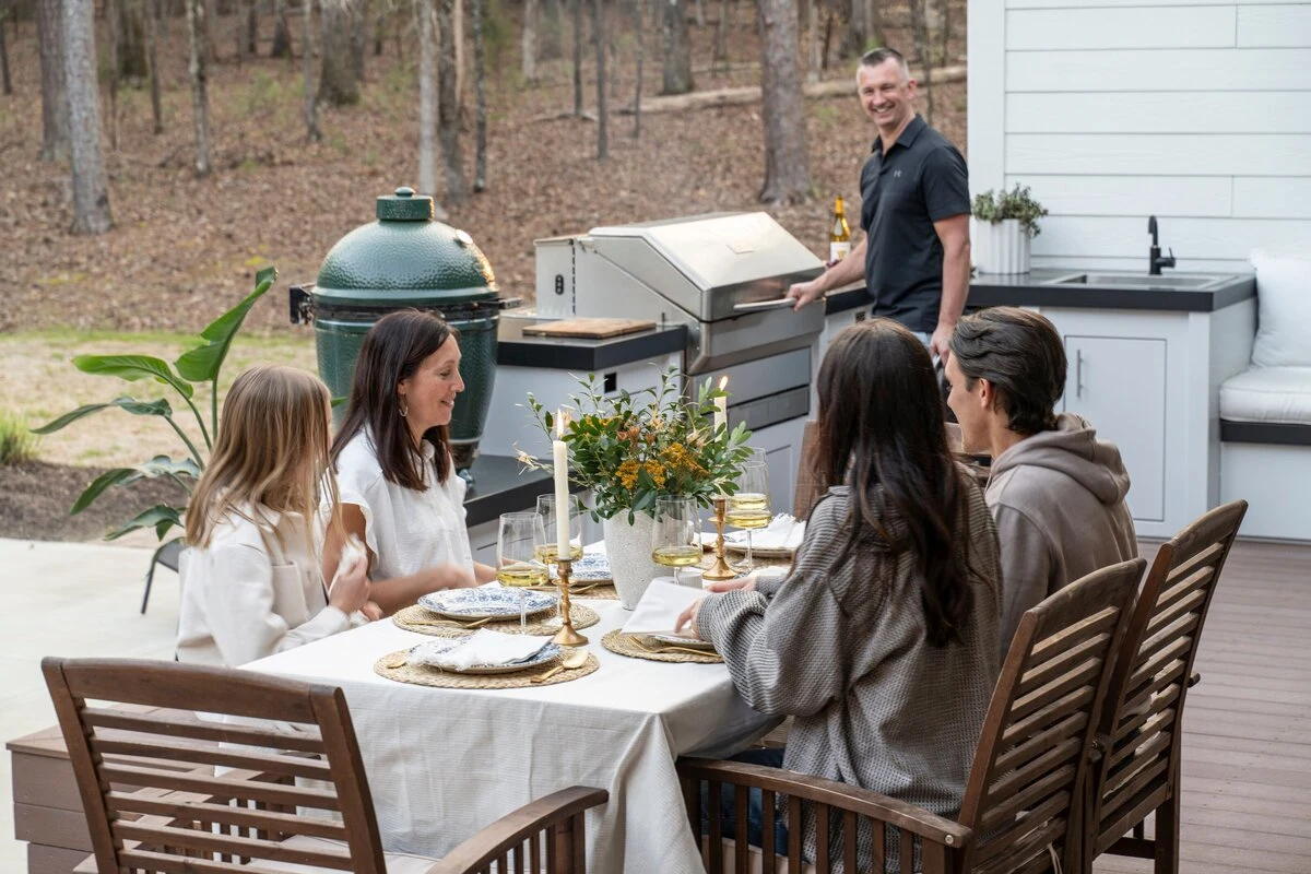 Custom outdoor kitchen with green egg grill and mixed seating at a dining table on a warm patio. Visit our Post Falls showroom.