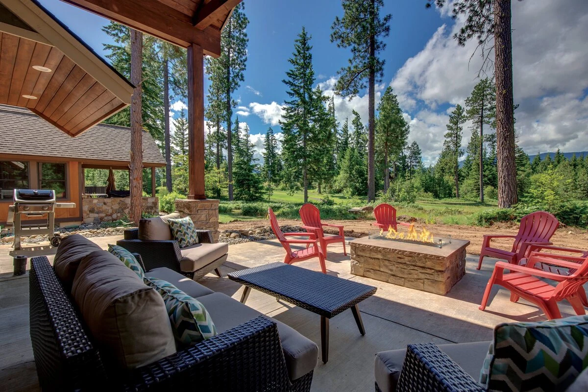 A rectangular fire pit with seating on a forested outdoor living space with tall pine trees in the background.