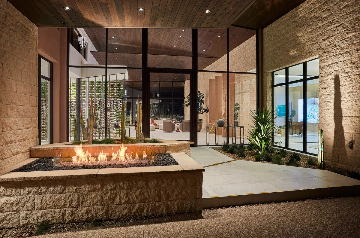 A rectangular linear fire pit set into a modern covered patio with floor-to-ceiling windows and outdoor seating.