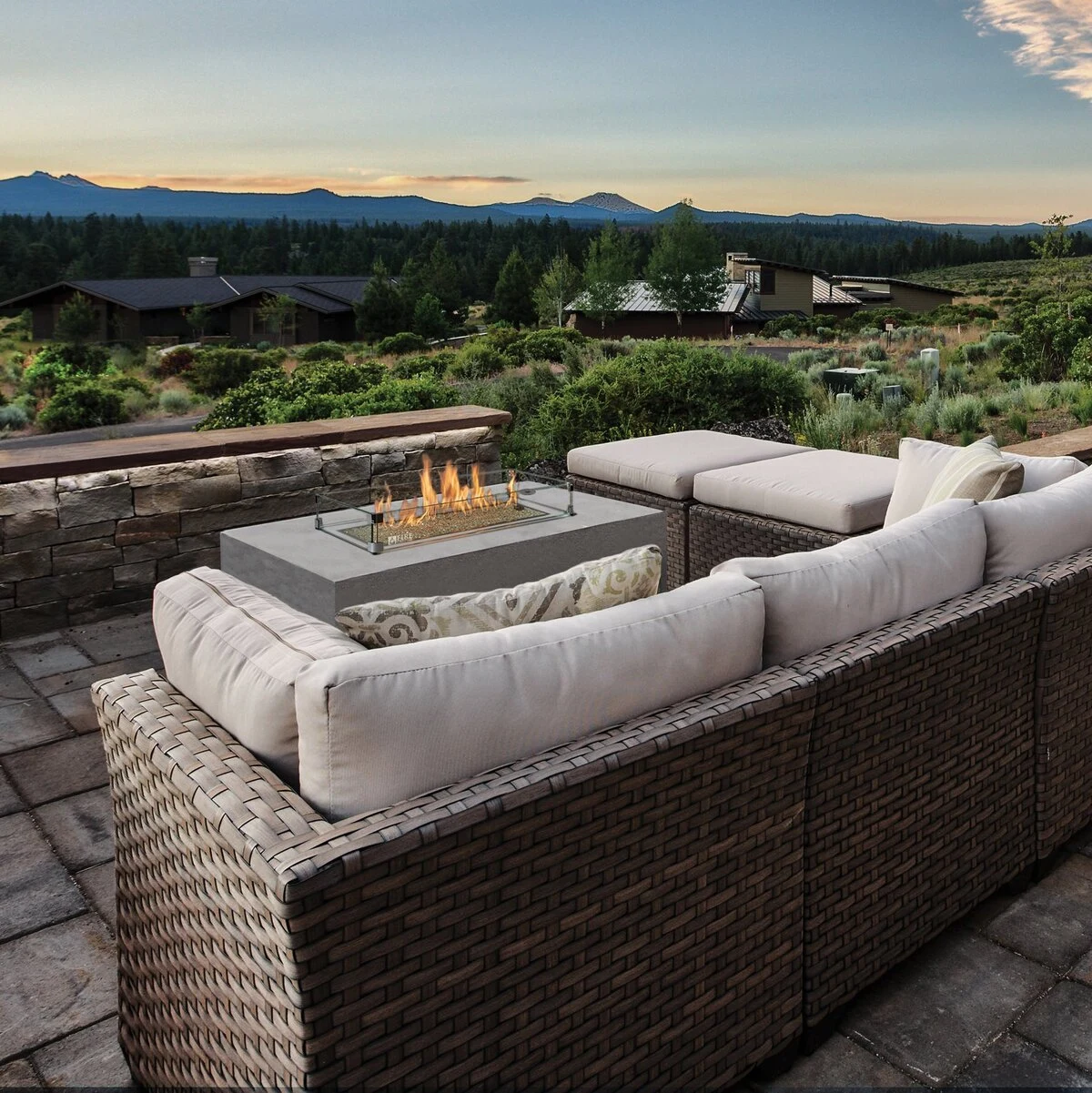A rectangular fire table with an active flame surrounded by gray outdoor sectional seating on a patio.