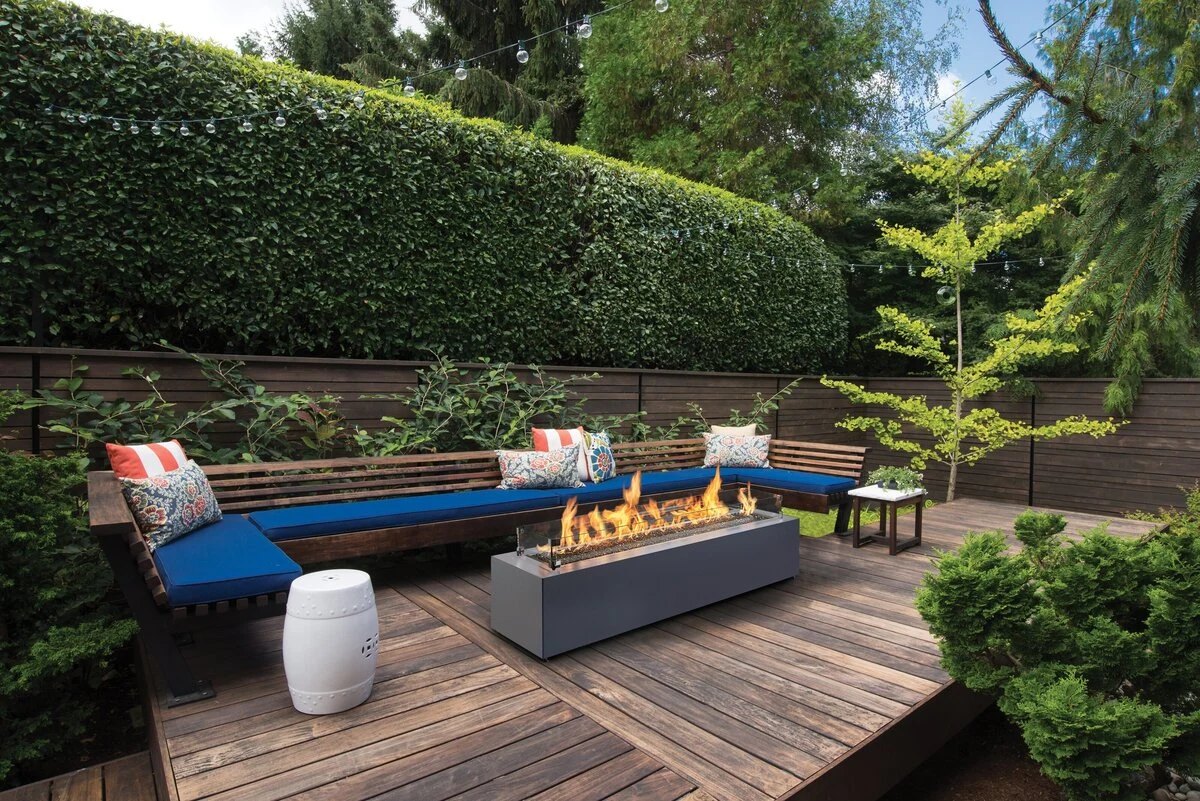 A rectangular linear fire table with an active flame set into a landscaped outdoor patio with stone pavers.