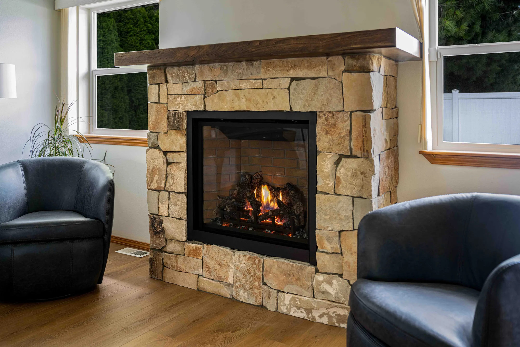 Stone gas fireplace flanked by windows and leather chairs