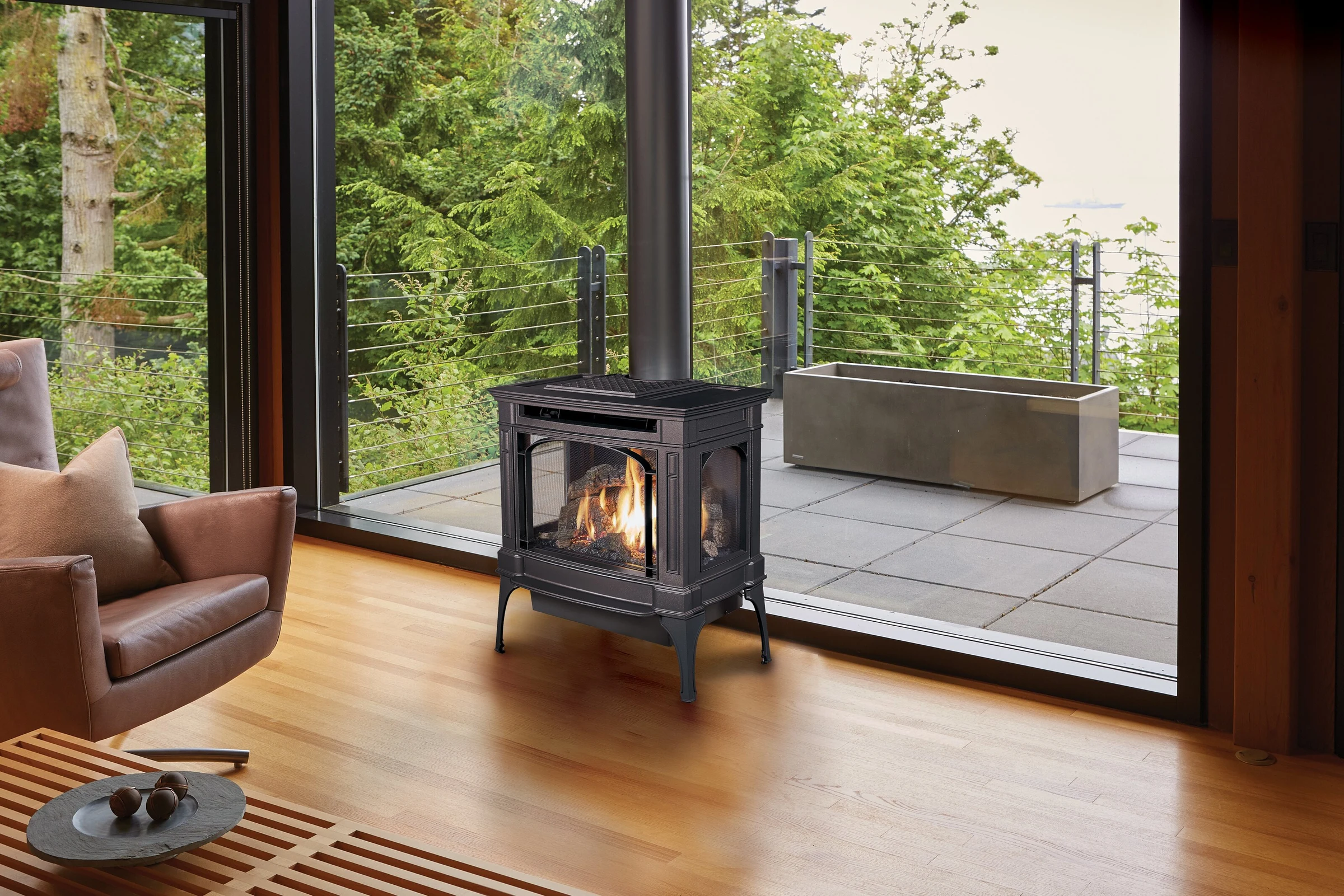 A Lopi Berkshire Bay Window gas stove on a hearth pad in a bright room with wood floors and floor-to-ceiling windows.