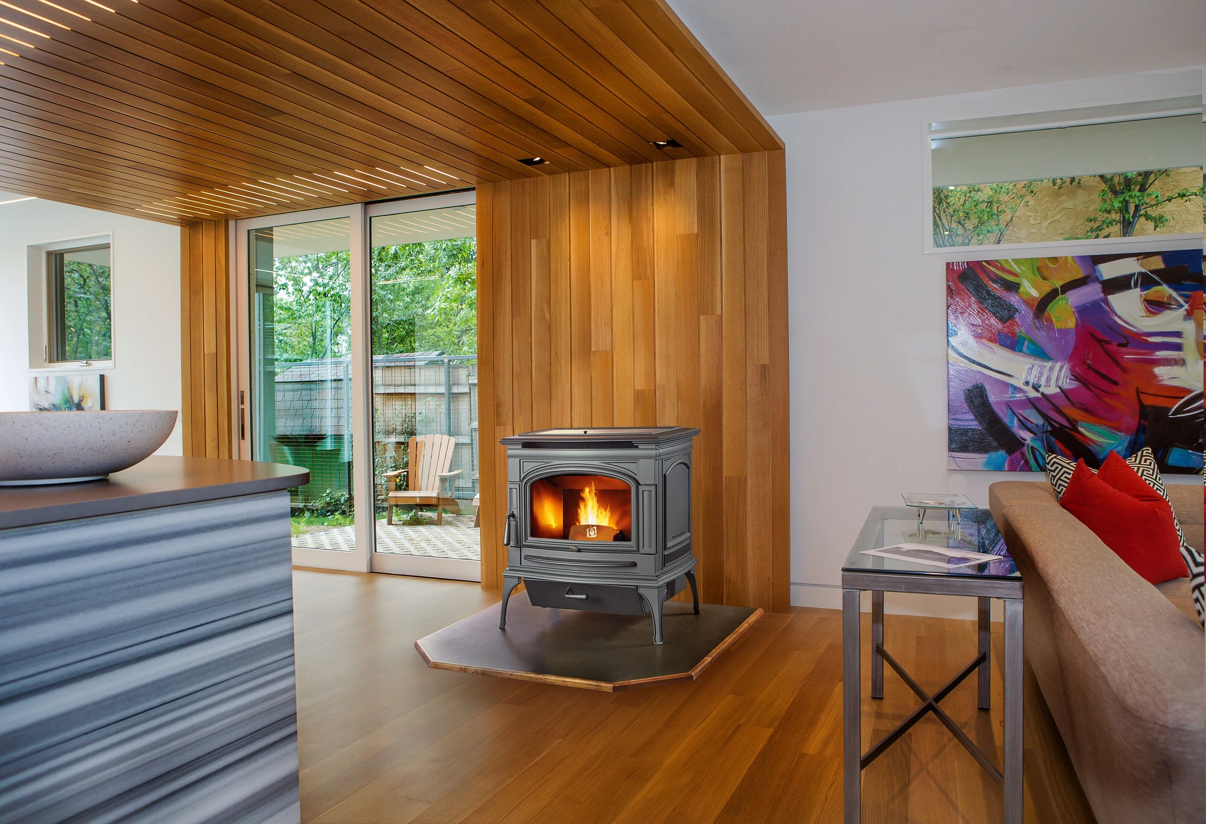 Lopi Deerfield Pellet Stove in a bright living room with hardwood floors and large windows overlooking trees.