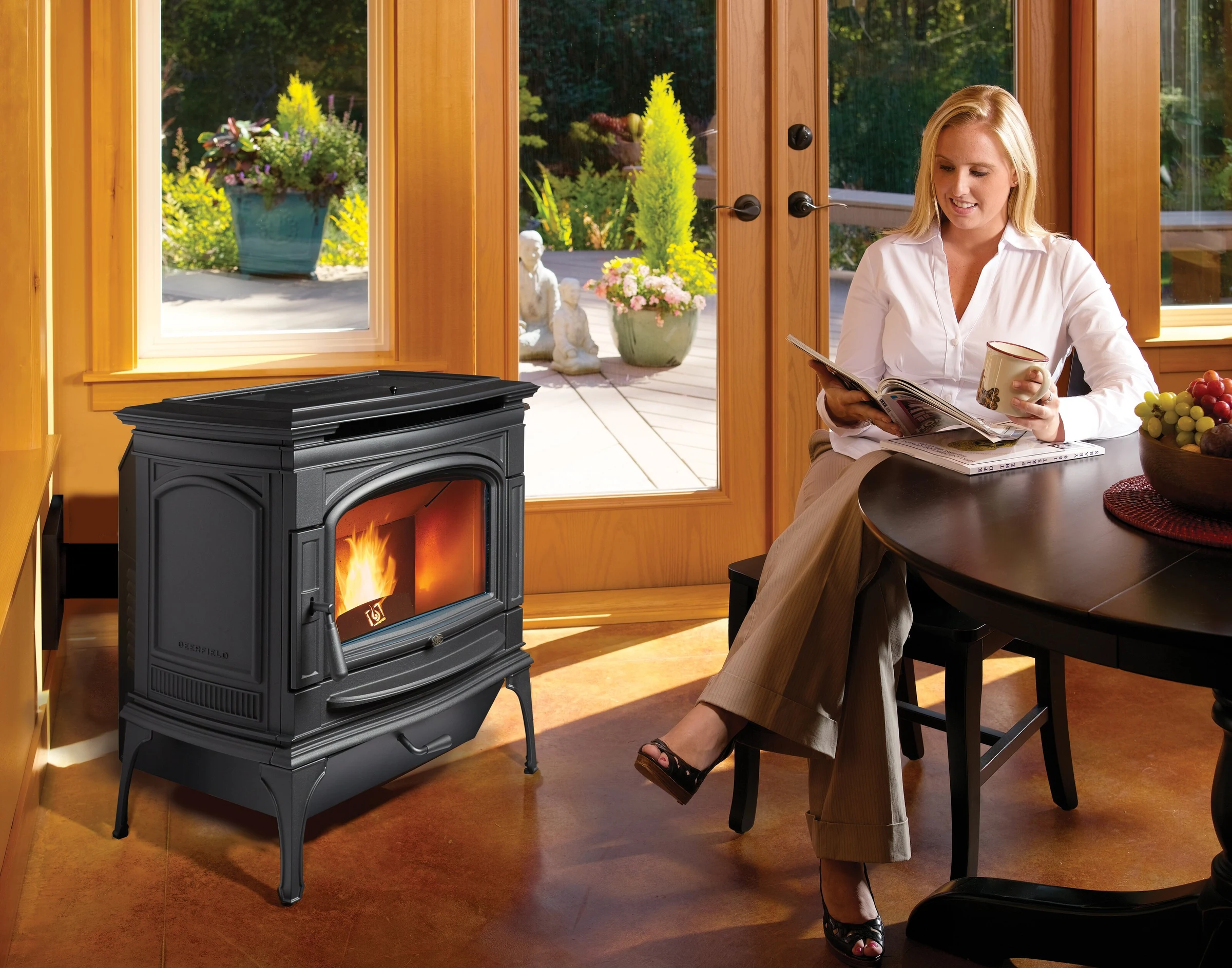 Lopi Deerfield Pellet Stove in a sunlit living room with hardwood floors and a woman relaxing in a nearby chair.