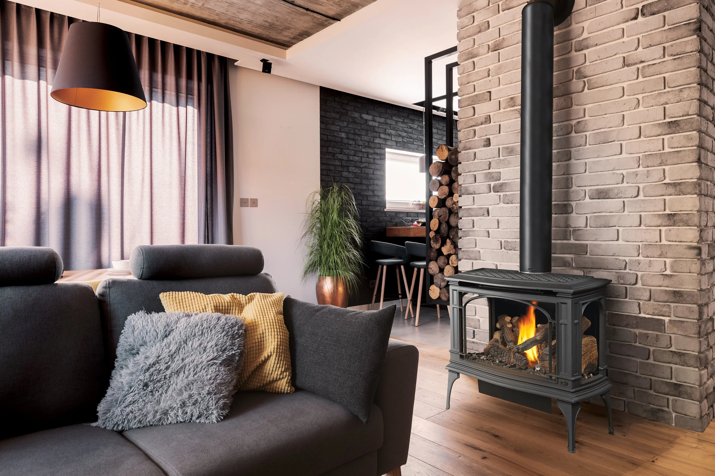 Lopi Greenfield Bay Window Gas Stove in a modern living room with a dark brick accent wall, gray sofa, and warm ambient lighting.