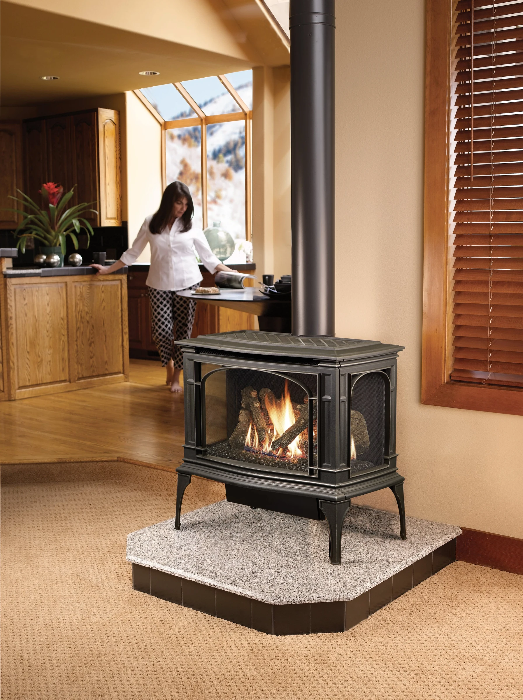 Lopi Greenfield Bay Window Gas Stove in a bright living space with wood cabinetry and a person visible in the background.
