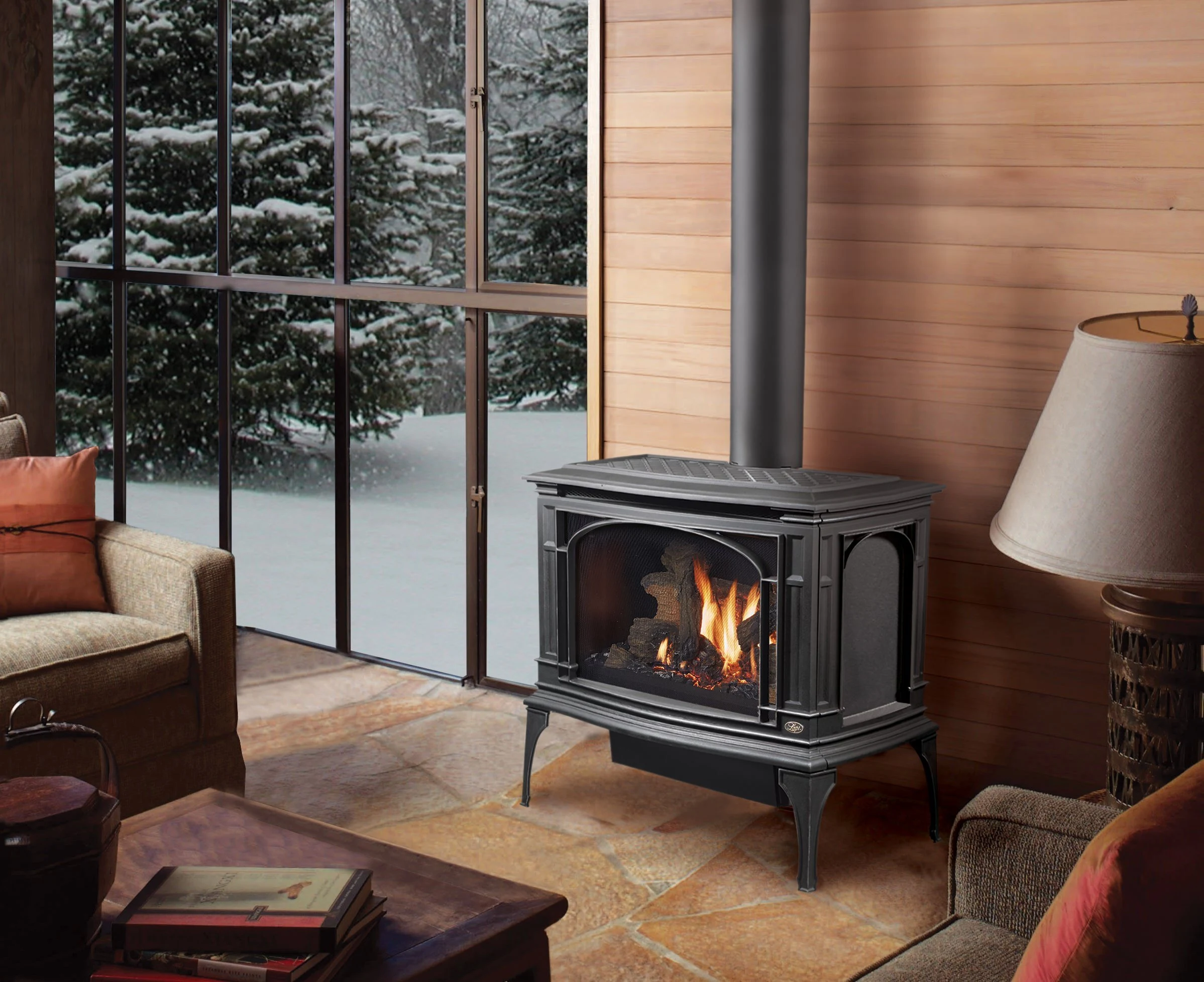 Lopi Greenfield Millivolt Gas Stove in a sunlit living space with large windows overlooking snowy trees and wood paneled walls.