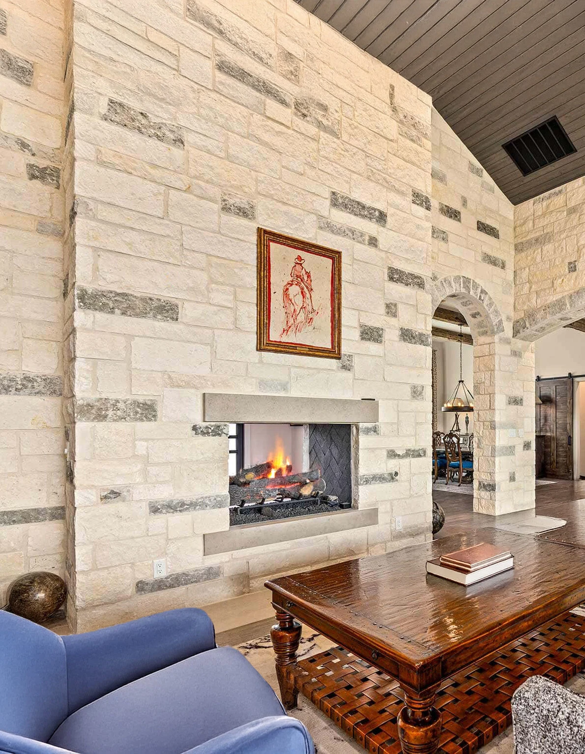 A linear gas fireplace set into a floor-to-ceiling white stone surround in a bright living room with a mounted TV above.