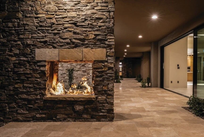 A masonry fireplace with a stacked stone surround and raised hearth in a warm, rustic living space.