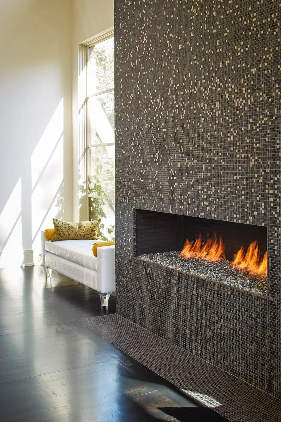 A linear gas fireplace set into a gray tile surround in a modern living room with neutral furnishings.