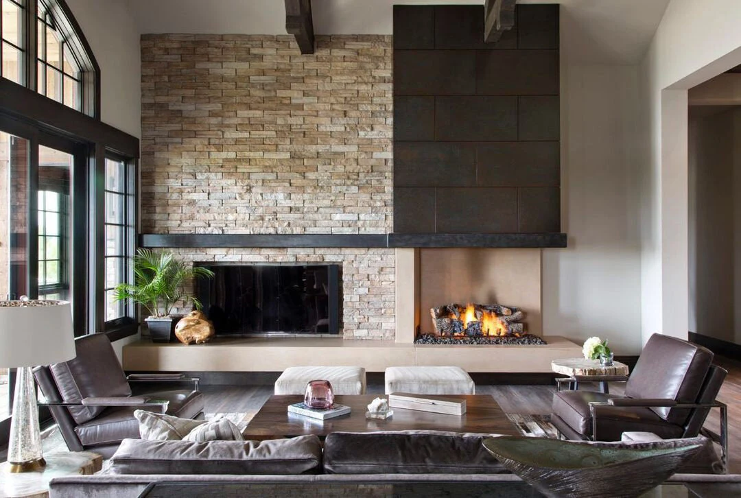 A masonry fireplace with a stacked stone surround and wood mantel in a warm contemporary living room.