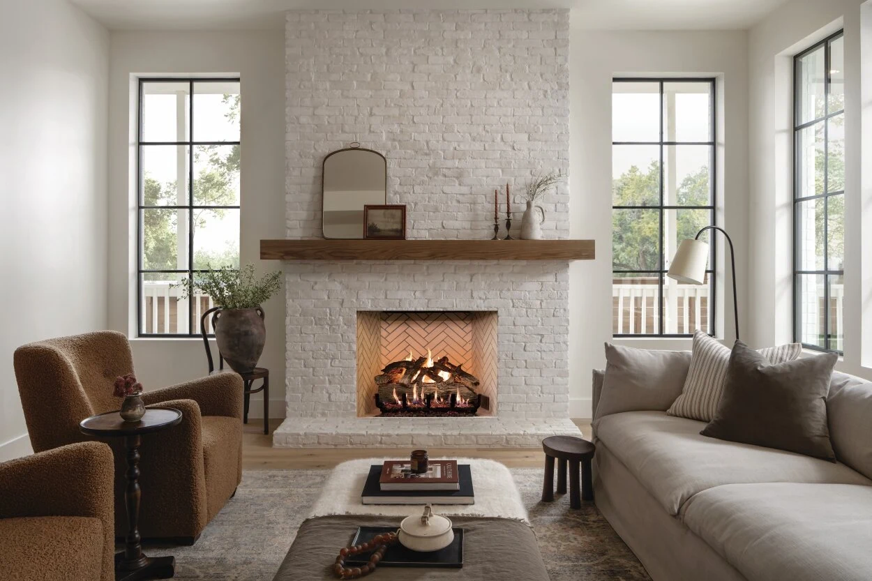 A linear gas fireplace set into a white wall with a floating wood mantel in a minimalist living room.