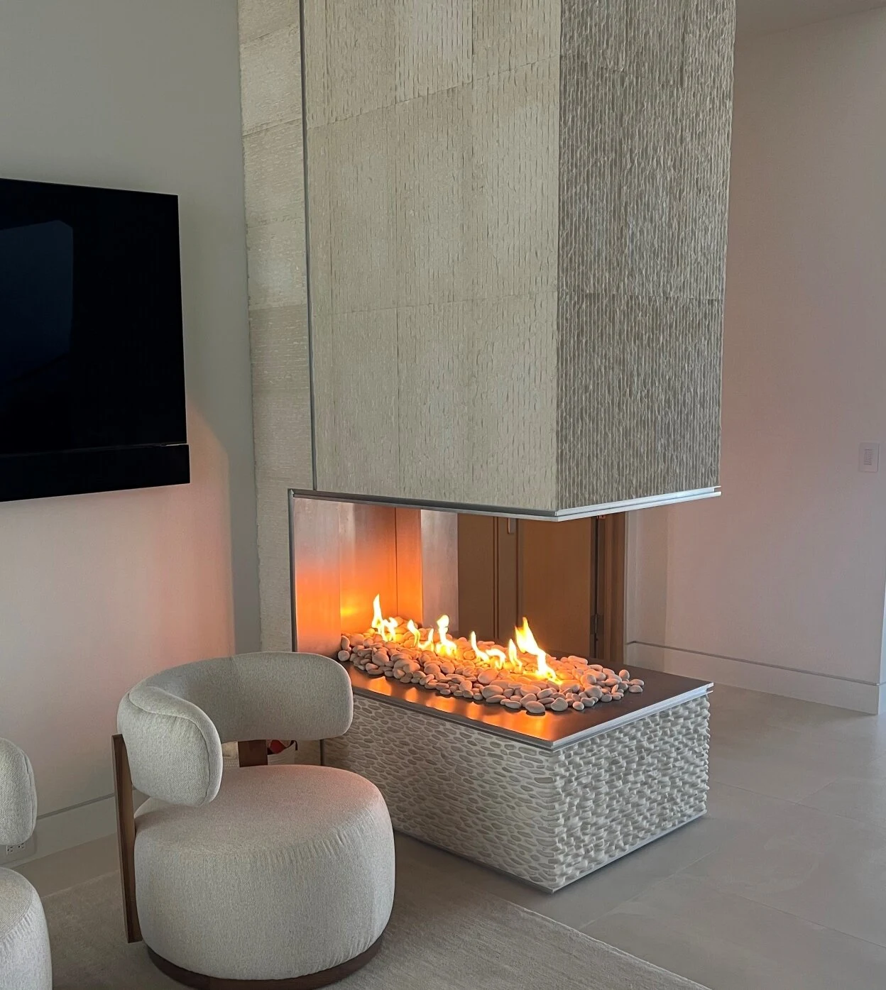 A linear gas fireplace set into a light gray surround in a modern living room with neutral furnishings.