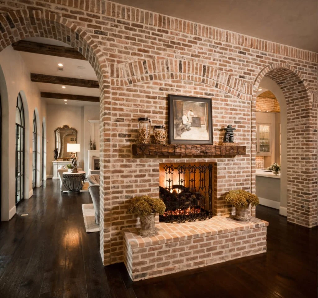 A masonry fireplace with a stacked stone surround and raised hearth in a warm living room with earth-toned furnishings.