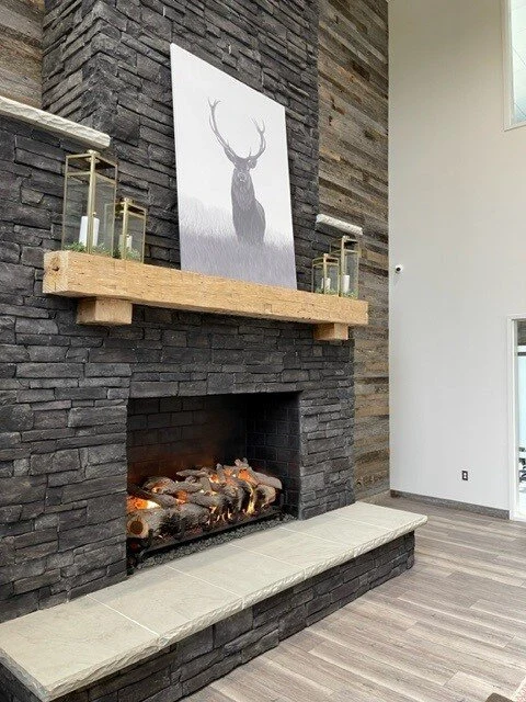 A masonry fireplace with a floor-to-ceiling stacked stone surround and wood mantel in a rustic living room.