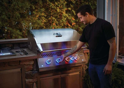 Napoleon Built-In 700 Series 32 grill with the lid open in an outdoor kitchen, control knobs glowing blue and red.