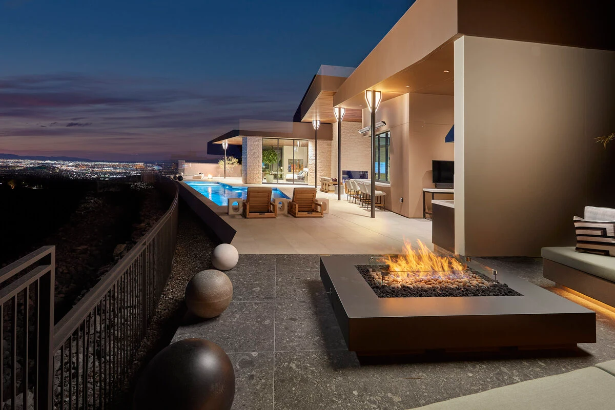 A rectangular fire table with an active flame surrounded by cushioned outdoor seating on a covered patio.
