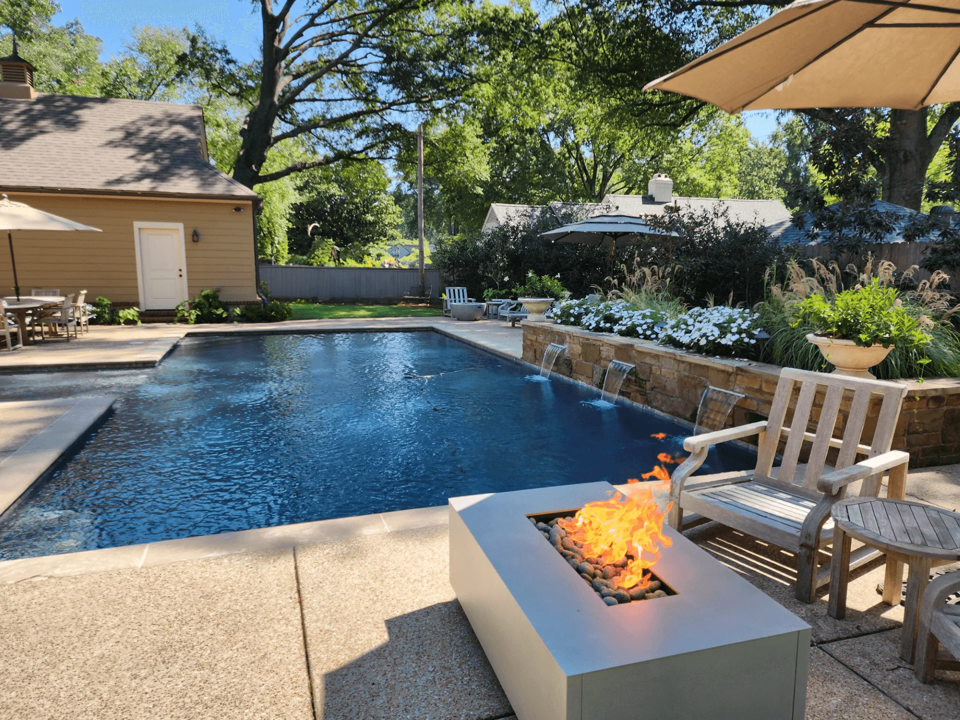 Warming Trends AON square fire table burning beside a backyard pool