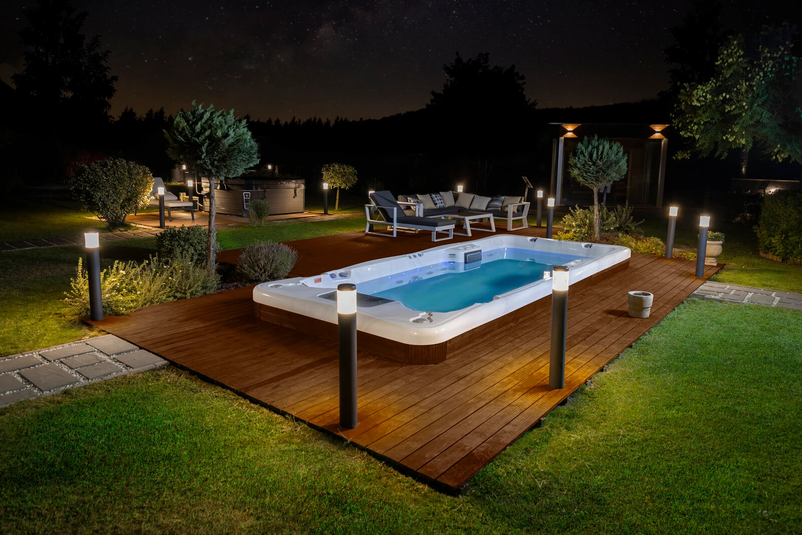 Wellis Amazonas W-Flow premium swim spa on an illuminated wooden deck at night