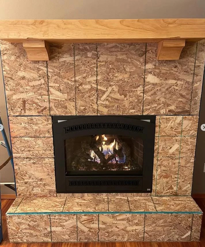 Cement backer board and solid wood mantel installed around a lit gas fireplace during installation