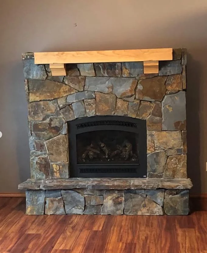 Natural stacked stone veneer hand-placed around a gas fireplace with a wood mantel