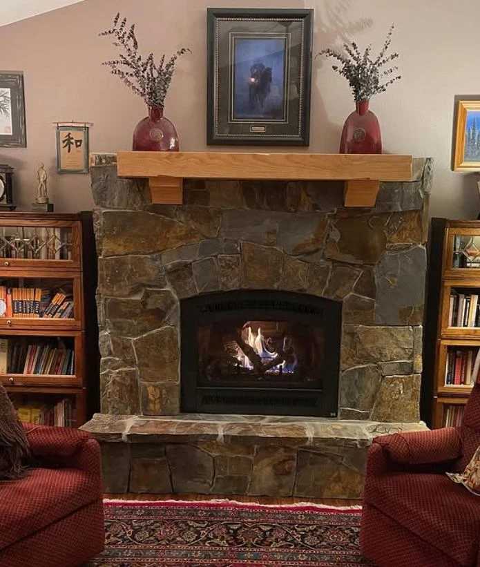 Finished custom stone fireplace with stained mantel and a fire burning in a cozy North Idaho living room