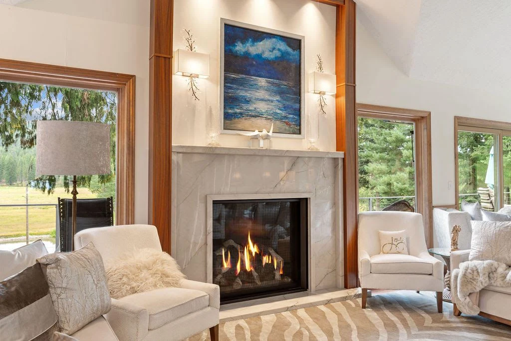 Elegant custom fireplace with a white marble surround and a lit fire in a bright North Idaho living room